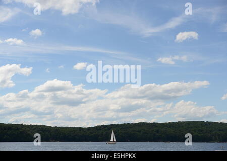 Sail Boat on Lake with mountains and a beautiful blue sky with white puffy clouds Stock Photo