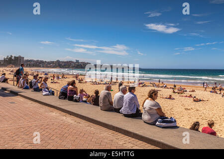 People sitting in a row on a wall and looking out over Manly Beach, Sydney, Australia. Stock Photo