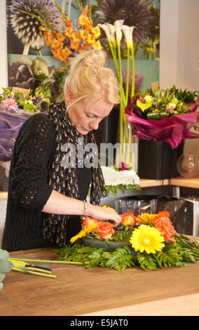 Florist arranging a wreath in a florist's shop with bunches of flowers and a flower poster in the background. Stock Photo