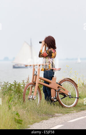 Netherlands, Venhuizen,  Bough Bike. The Dutch Design wooden bike. Woman looking at sailing boat with binoculars Stock Photo