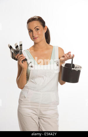 Attractive female painter wearing bib & braces overall holding brush and paint pot Stock Photo