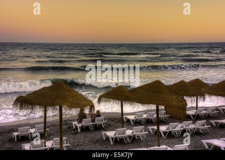 Two people sitting on a sun lounger at dusk on the Playa El Salon beach in Nerja Spain Stock Photo