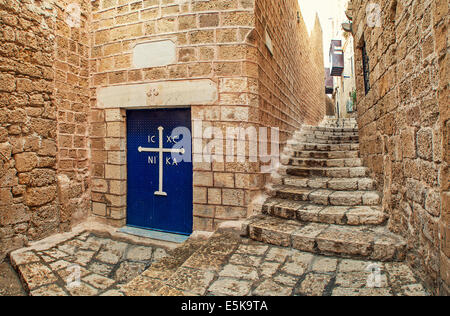 Metal door with white cross at the entrance to small church and narrow stone streets in Jaffa, Israel. Stock Photo