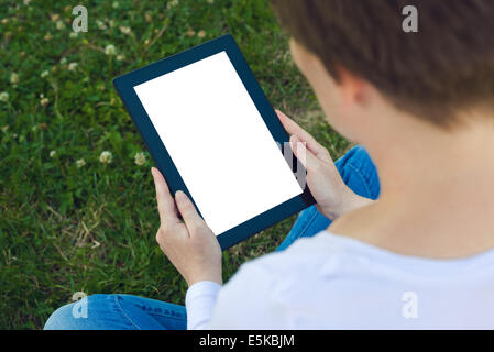 Woman holding digital tablet computer with blank white screen and browsing the internet while sitting on green grass in the park Stock Photo