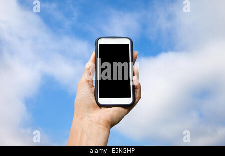 Generic cell phone held by female hand against blue sky with clouds. Stock Photo