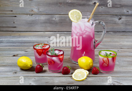 Front view of freshly made pink lemonade with whole lemons, strawberries and filled glasses on rustic wood Stock Photo