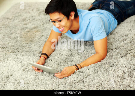 Happy asian man lying on the carpet with tablet computer Stock Photo