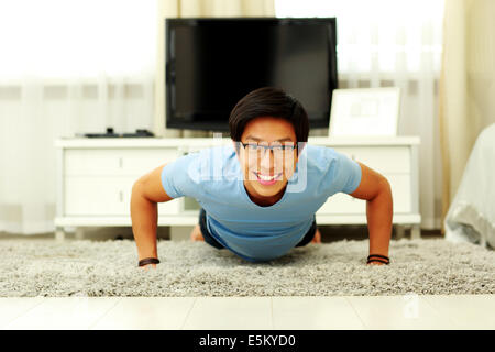 Portrait of a smiling  young man doing push ups in the living room at home Stock Photo