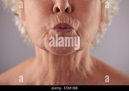 Close-up portrait of mature woman puckering lips against grey background. Senior woman grimacing. Focus on lips. Stock Photo