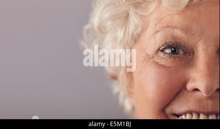 Part of senior woman face with focus on grey eyes. Old woman face close-up with copy space on against grey background.