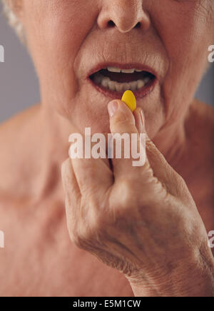 Cropped image of old woman taking a pill. Focus on hand and pill. Close-up of senior woman taking medication for good health. Stock Photo