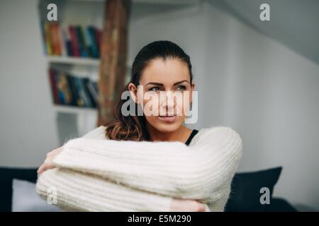 Portrait of young lady sitting alone on sofa looking away. Caucasian female model at home daydreaming. Stock Photo