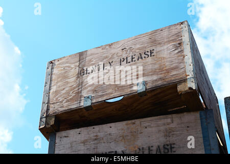 Wooden fruit boxes stacked high against a blue sky, labelled with the words GENTLY PLEASE. Stock Photo