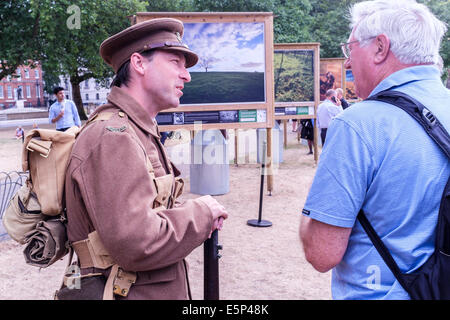 London, UK, 4th August 2014. Fields of Battle, Lands of Peace, an exhibition of photographs by  Michael St. Maur Sheil  is officially opened in St. James's park. Sponsored by The Royal British Legion the exhibition is on display directly opposite Horse Guards, adjacent to the Guards Memorial until Armistice Day on November 11th. Pictured A storyteller dressed in WW1 uniform of British soldiers discusses with visitors what life was like for the men in the trenches during the conflict. Credit:  mark phillips/Alamy Live News Stock Photo