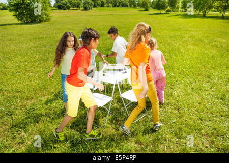 Kids run around playing musical chairs game Stock Photo