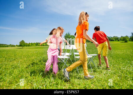 Children run around chairs playing a game outside Stock Photo