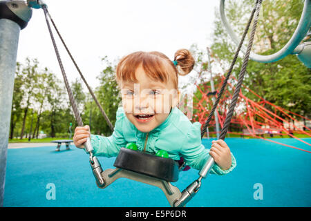 Excited girl on swing holding it with ropes Stock Photo