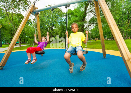 Boy and girl sitting on the swings together Stock Photo