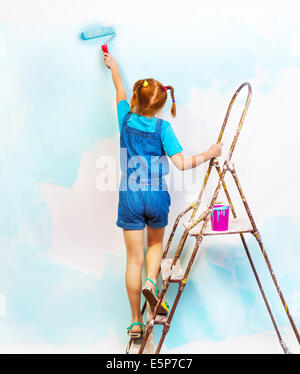 Little girl in bib and brace stands on a ladder Stock Photo