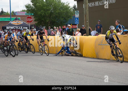 Two racers crash as they speed around 'crash corner' on a lap of the criterium in the community of Bowness. A criterium is a fast cycling race on a short circuit with the city streets closed to traffic. This bicycle street race is part of the three-race Tour de Bowness. Calgary, Alberta, Canada. Stock Photo