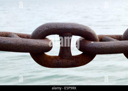 Closeup of large steel brown rusted chain link against water. Stock Photo