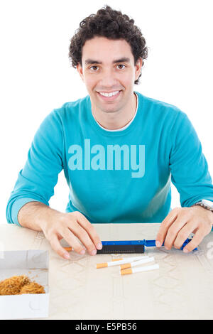Smiling man in blue sweater making cigarettes with device for cigar and dry tobacco on table Stock Photo