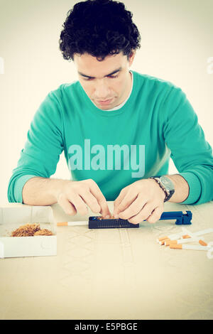 Young man preparing cigars and rolling tobacco in sticky paper with filters Stock Photo