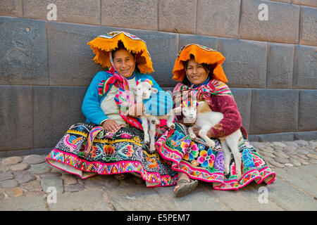 Two Quechua women in traditional dress holding lambs in their arms, sitting on the ground, Cusco Province, Southern Peru, Peru Stock Photo