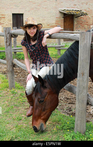 Cowgirl sitting on a fence near a horse Stock Photo