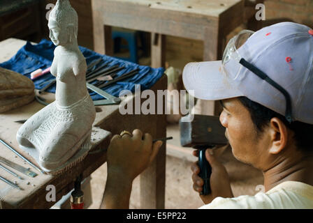 Sculptor at work at Artisans d'Angkor, Siem Reap, Cambodia. Young Cambodian artisan during the artistic craftsmanship of stone with a wooden hammer and a chisel to produce a traditional. Stock Photo