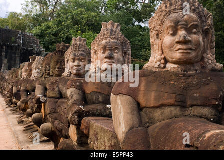 Carved stone warrior gods along the bridge over the moat near the South entrance to Angkor Thom. Detail of stone heads on bridge entering Angkor Thom, Cambodia. South gate to angkor thom in Cambodia is lined with warriors and demons. Stock Photo