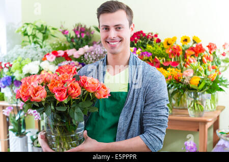 Young handsome florist selling flowers and bouquets in shop Stock Photo