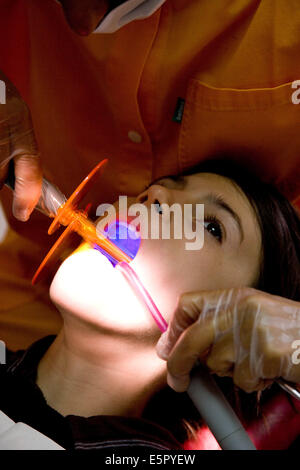 13 year old child receiving dental care. The dentist uses ultraviolet light to polymerize a photosensitive filling. Stock Photo