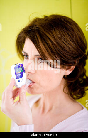Woman using a PIKO-6, a digital peak flow meter mesuring the volume of expired air. Stock Photo