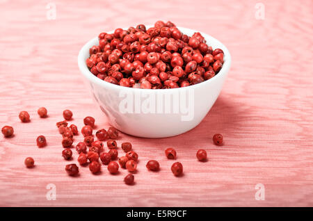 Pink Pepper - Dried pink peppercorns in a white porcelain bowl on pink textile made of linen. Stock Photo