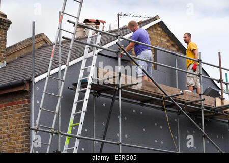 Builders attaching / fitting rigid foam wall insulation sheets / panels / boards to the gable end of Victorian terraced house UK Stock Photo