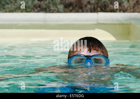 Teenager boy submerged wearing diving mask or goggles in swimming pool. Stock Photo