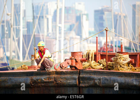 Asian Engineer Supervises The Dredging Of The Causeway Bay Typhoon Shelter, Hong Kong Cityscape Behind. Stock Photo