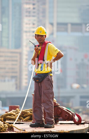 Asian Engineer Supervises The Dredging Of The Causeway Bay Typhoon Shelter, Hong Kong Cityscape Behind. Stock Photo