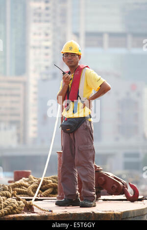 Asian Engineer Supervises The Dredging Of The Causeway Bay Typhoon Shelter, Hong Kong Cityscape Behind. Stock Photo