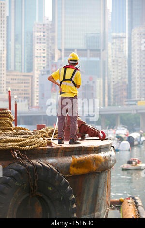 Asian Engineer Supervises The Dredging Of The Causeway Bay Typhoon Shelter, Hong Kong Cityscape Behind. Stock Photo