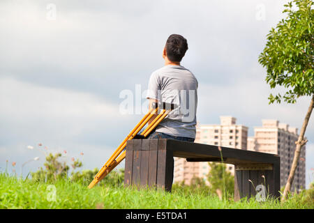 Injured Man with Crutches sitting on a bench Stock Photo