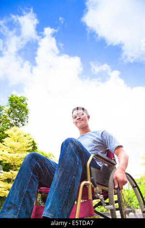 smiling young man sitting on a wheelchair with natural background Stock Photo
