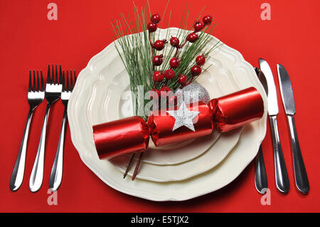 Modern bright red Christmas table setting with cracker and baubles, plates and cutlery, on a red tablecloth background. Stock Photo