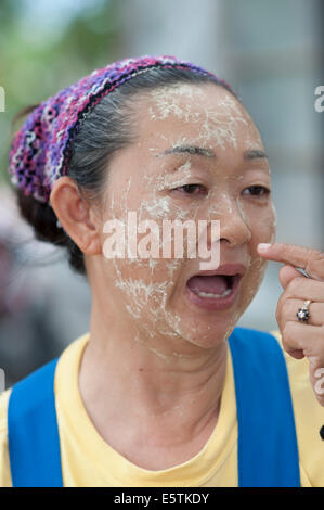 An elderly Thai woman using natural herb and leaf mixture to protect her face from the sun Stock Photo