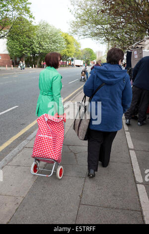 Woman in Bright Green Coat Pulling Red Spotty Shopping Trolley Stock Photo