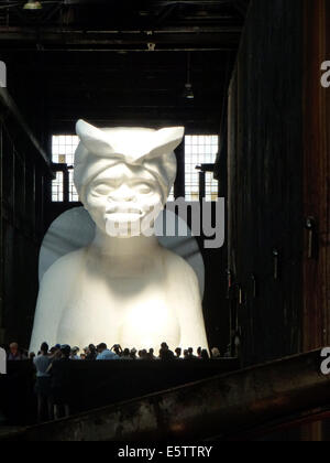 Visitors look at a white sphinx made of sugar by African American artist Kara Walker in the former Domino sugar factory in Williamsburg, Brooklyn, New York, USA, 22 June 2014. The 23 meters long, eight meters wide and eleven meters high sculpture is part of the exhibition 'A Subtlety or the Marvelous Sugar Baby'. Photo: Alexandra Schuler Stock Photo