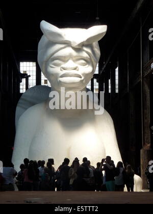 Visitors look at a white sphinx made of sugar by African American artist Kara Walker in the former Domino sugar factory in Williamsburg, Brooklyn, New York, USA, 22 June 2014. The 23 meters long, eight meters wide and eleven meters high sculpture is part of the exhibition 'A Subtlety or the Marvelous Sugar Baby'. Photo: Alexandra Schuler Stock Photo