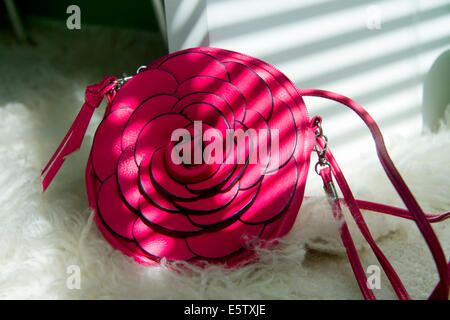 Decorative red leather handbag shaped like the petals of a flower on a lambs wool rug with patterned light from a venetian blind covered window Stock Photo