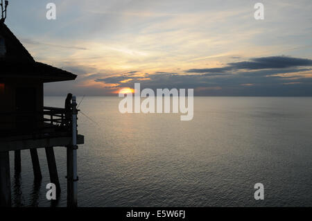 A lone fisherman tries his luck at sunset from Naples Pier, Florida Stock Photo